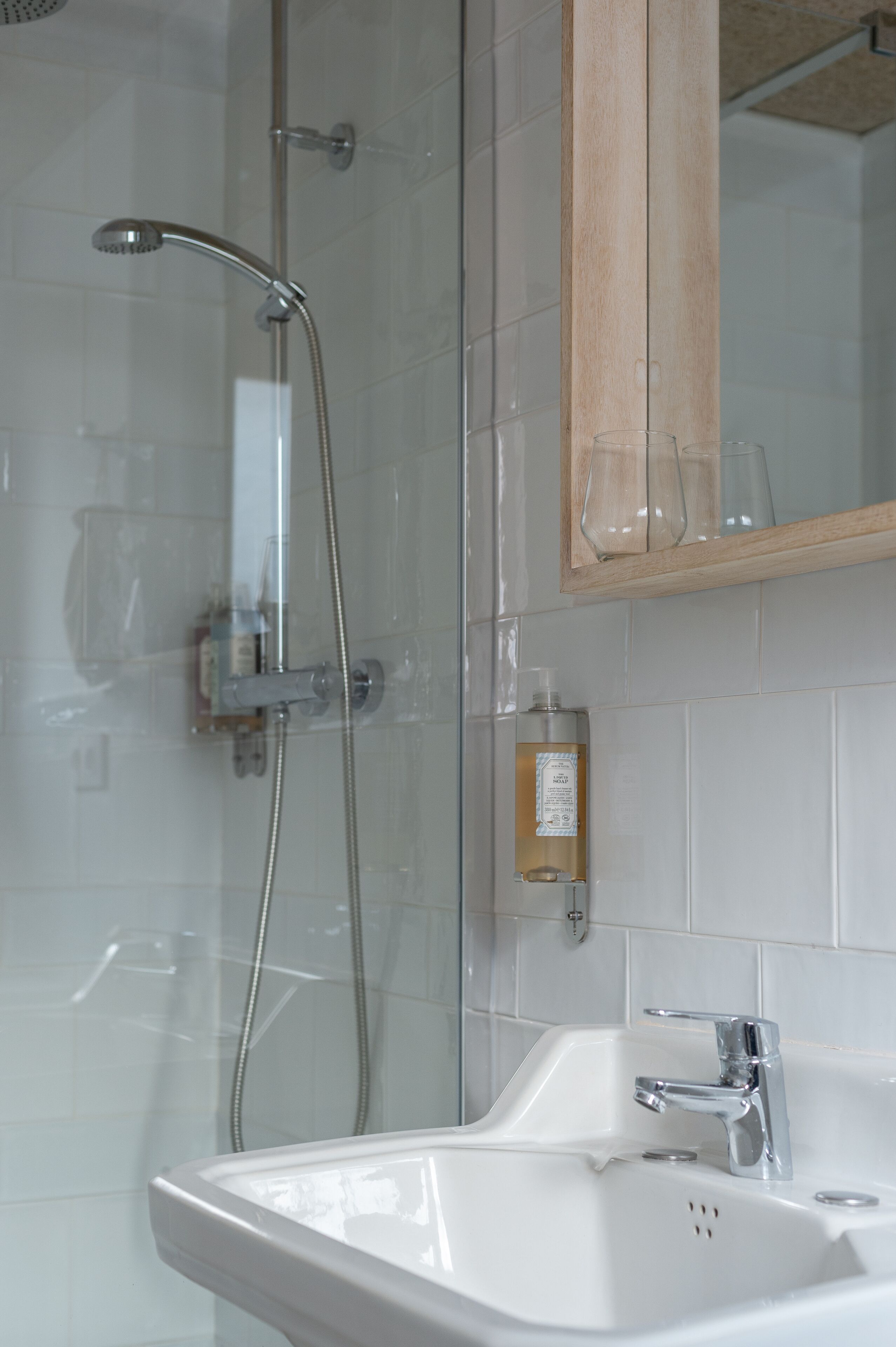 A bathroom with a shower, a sink, and a wooden medicine cabinet above the mirror.