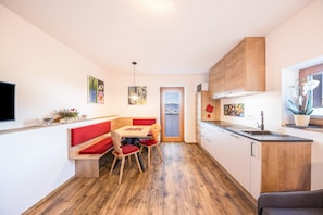 A modern kitchen with wooden cabinets, a dining area with a bench, and a view through a door.