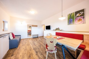 A modern room with a wooden floor, a dining table with benches, a sofa, and a TV mounted on the wall.