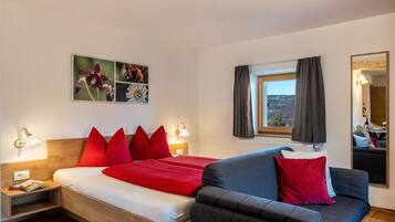 Un dormitorio con cama, mesitas de noche, un sofá, una ventana con cortinas y una obra de arte colgada en la pared.