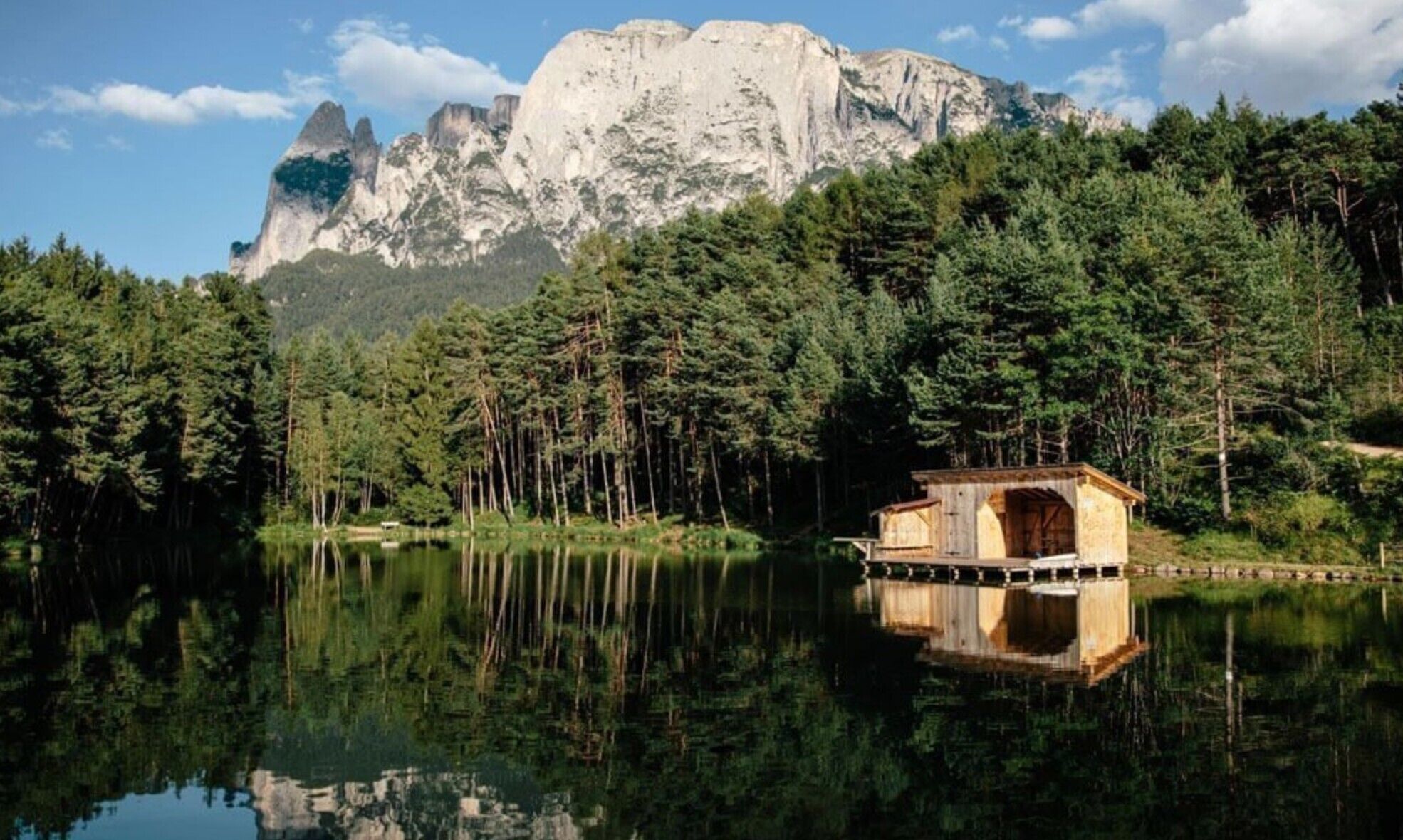 Una cabaña de madera junto a un lago, con una montaña al fondo.