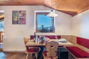 Ein Essbereich mit einem Holztisch, roten gepolsterten Bänken, einem Fenster mit Blick und einem an der Wand hängenden Kunstwerk.