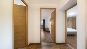 A hallway with wooden flooring, a wooden door on the left, and a bed with a wooden headboard on the right. - Apartment “Ritten Gfliererhof” with Mountain View, Garden & Balcony (Völs am Schlern)