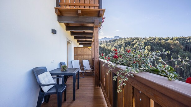 A balcony with wooden railings, a table with chairs, and a view of a forested mountain range. - Apartment “Ritten Gfliererhof” with Mountain View, Garden & Balcony (Völs am Schlern)