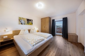 A bedroom with a bed, wooden wardrobe, bedside table, wall art, and a window with curtains.