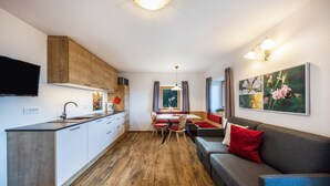 Et moderne køkken med træskabe, et spiseområde med bord og stole, samt en opholdsstue med sofa og fjernsyn.
