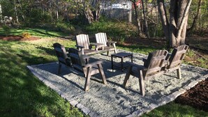 Une terrasse avec des fauteuils Adirondack et une table, entourée d’arbres et d’une pelouse.