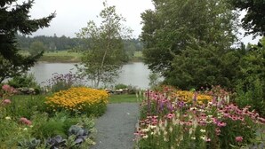 Un sentier de jardin qui mène à un lac, bordé de différentes espèces de fleurs et d’arbres.