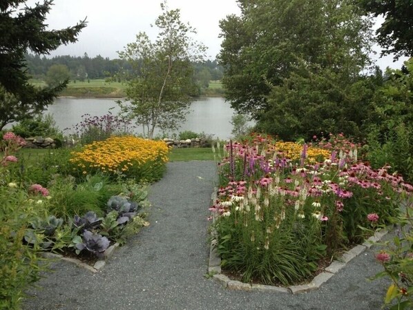 Un sentier de jardin qui mène à un lac, bordé de différentes espèces de fleurs et d’arbres.