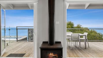A room with a wood-burning stove, a glass door leading to a balcony with a view of the sea, and a white interior.