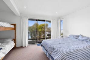 A bedroom with a bunk bed, a single bed, and a balcony with a view of trees.