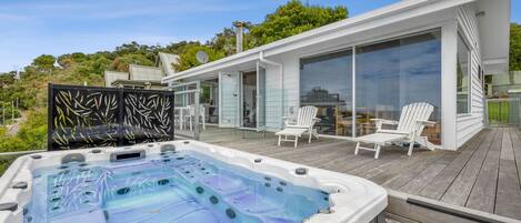 A hot tub on a wooden deck with glass doors leading to a covered outdoor area.