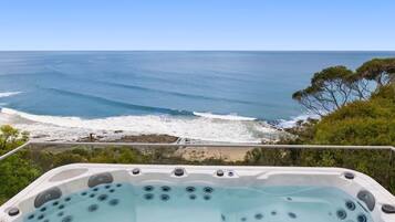 Relax in a hot tub on a balcony overlooking the ocean and lush surroundings.