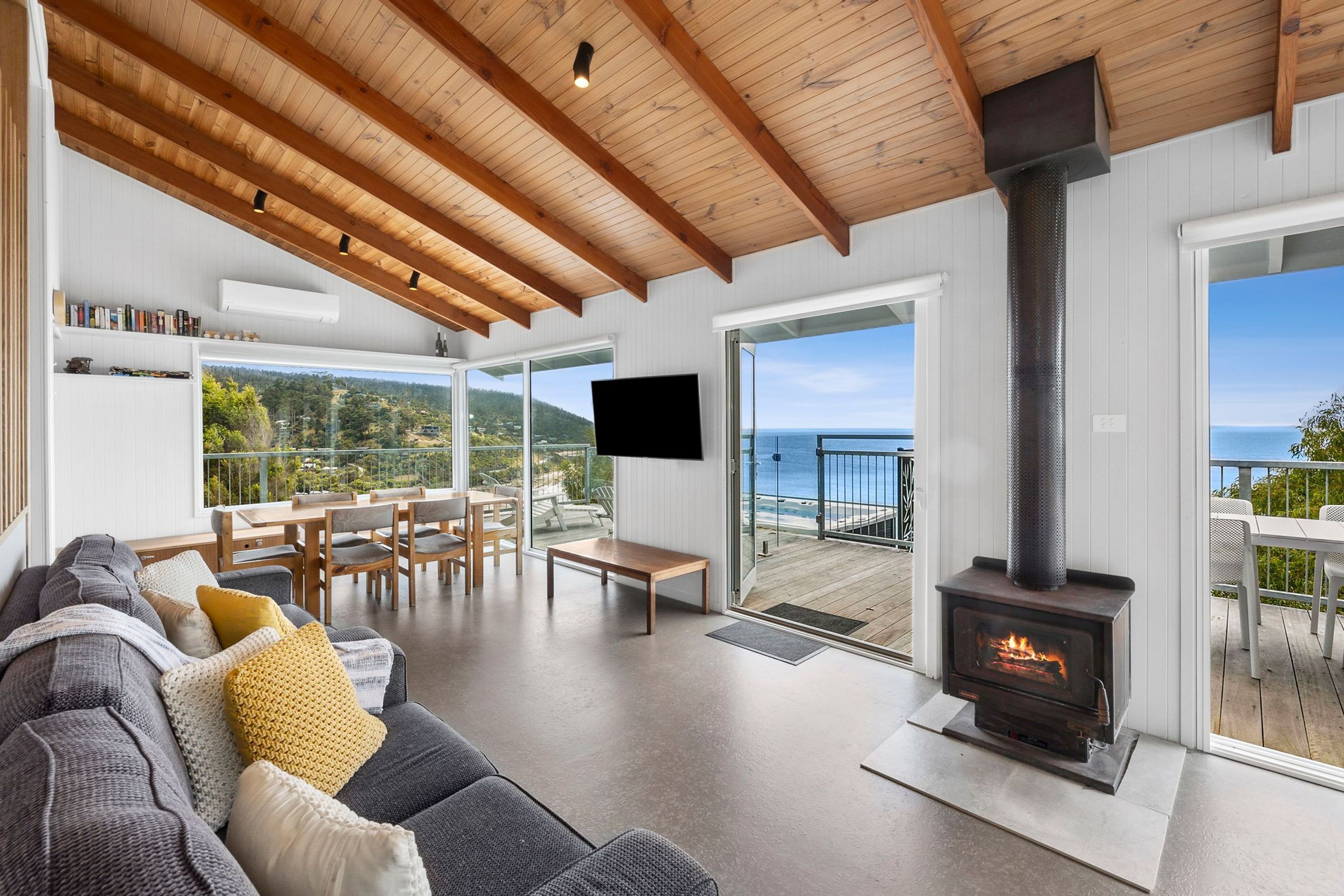 A modern living room with a fireplace, a sofa, a TV, and a balcony with a view of the sea.