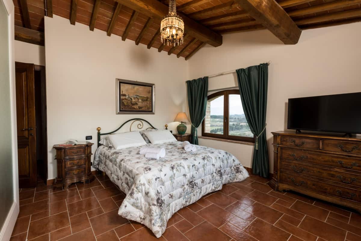 A bedroom with a bed, wooden dresser, TV, and a painting on the wall.