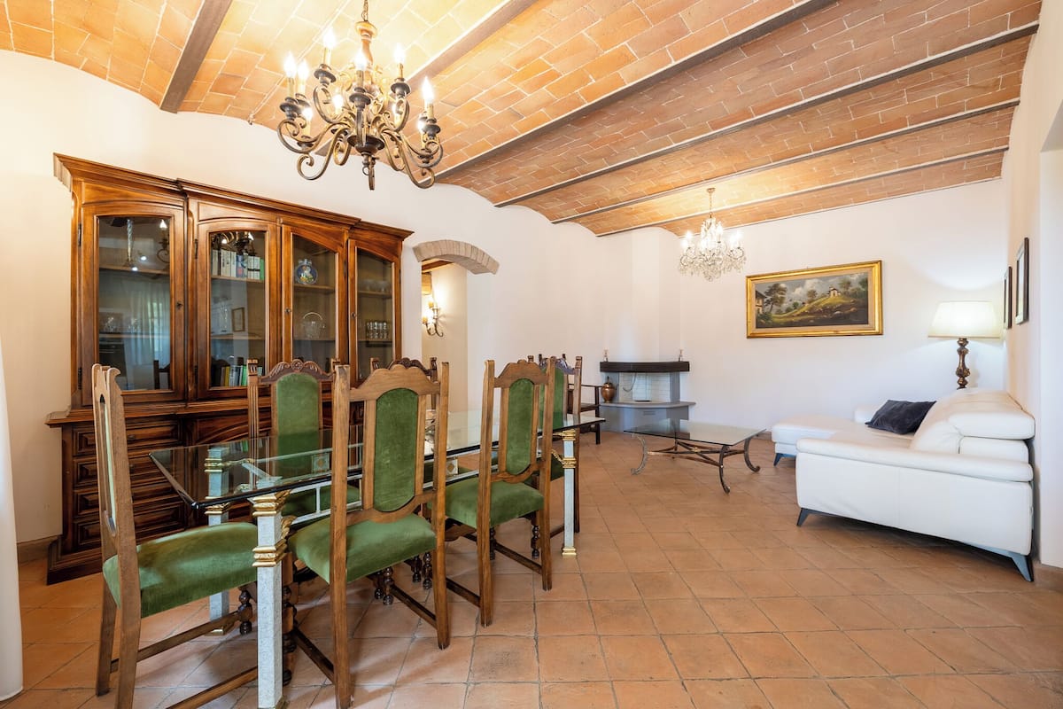 A dining area with wooden chairs and a glass table, a white sofa, and a fireplace.