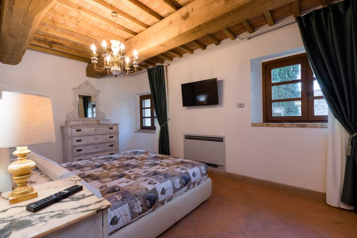 A bedroom with a bed, a dresser, a TV, a window with curtains, and a chandelier.