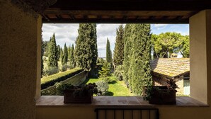 A view from a window overlooking a well-maintained garden with tall trees and a tiled-roof building. - Tenuta Tegolato (Barberino Tavarnelle)