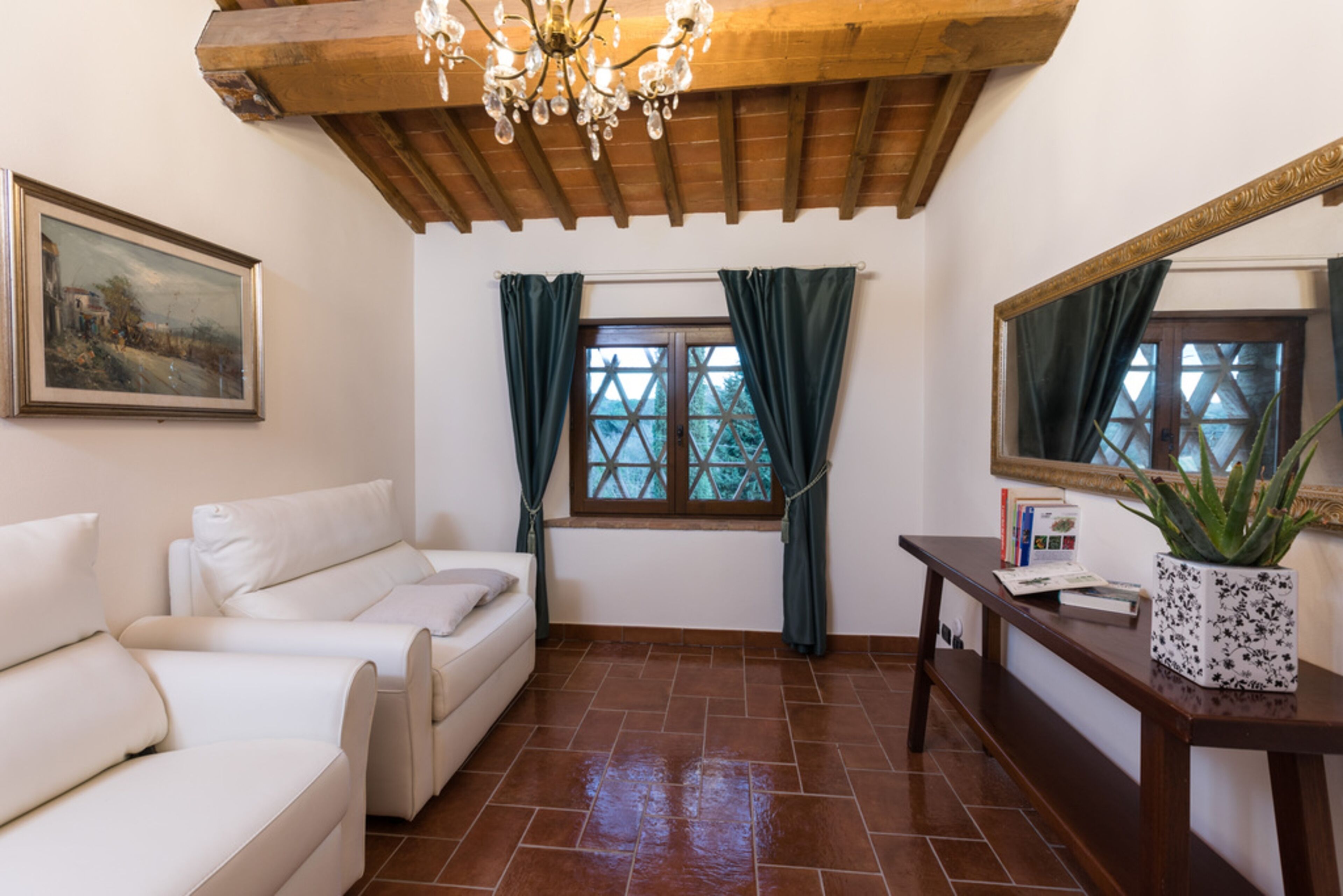 A room with a wooden ceiling, a white sofa, a window with curtains, a mirror, and a potted plant.