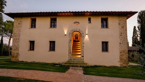 A two-story building with a stone facade, a central arched entrance, and a brick pathway leading to the entrance. - Tenuta Tegolato (Barberino Tavarnelle)