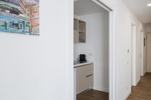 Un pasillo estrecho con una zona de kitchenette que incluye una cafetera, un estante pequeño con tazas y un lavavajillas.