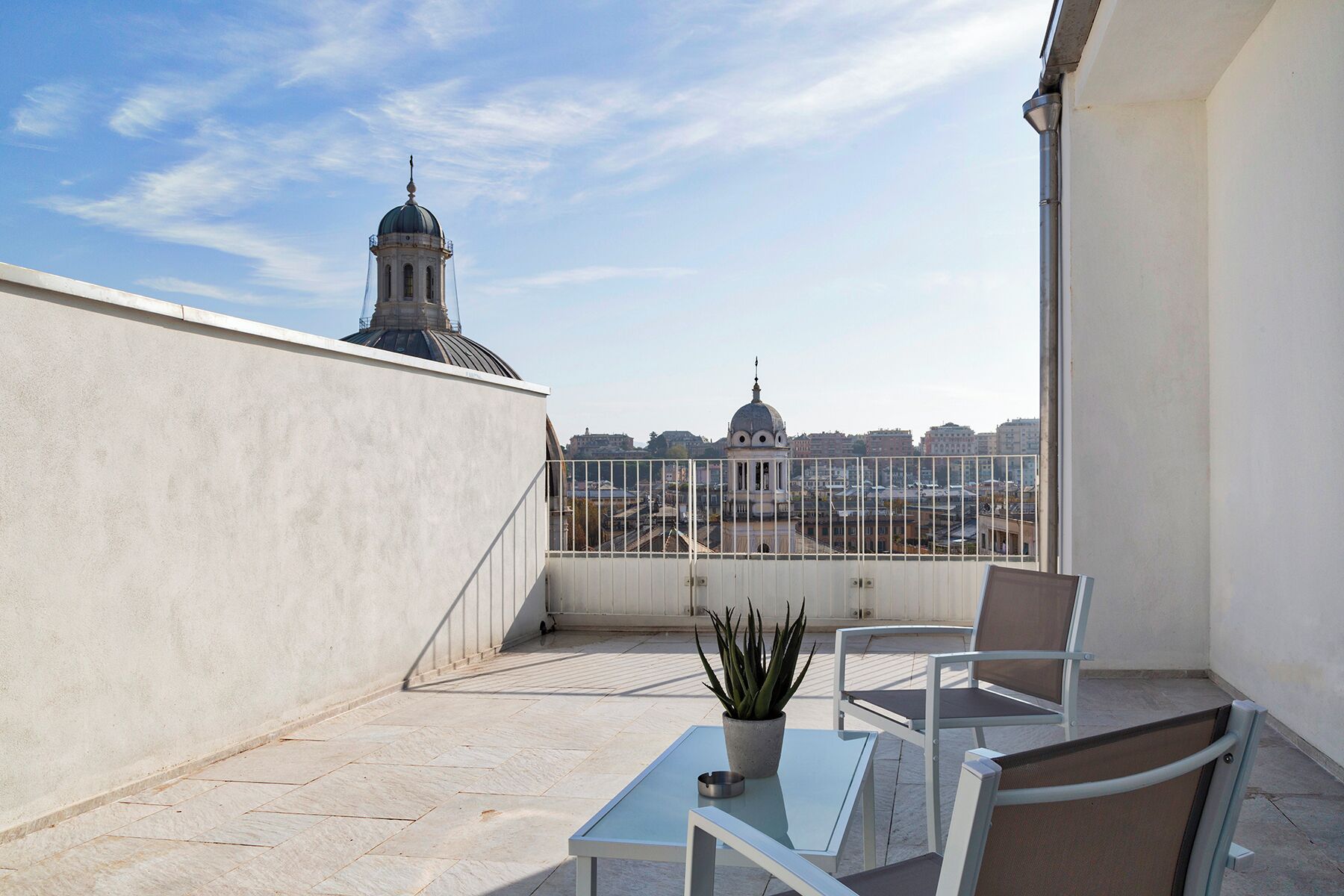 A rooftop terrace with a table and chairs, a potted plant, and a view of city buildings.