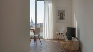 A modern living room with a large window, a dining area with chairs, a television, and a framed artwork on the wall. - Deluxe Apartments by Wonderful Italy (Genoa)