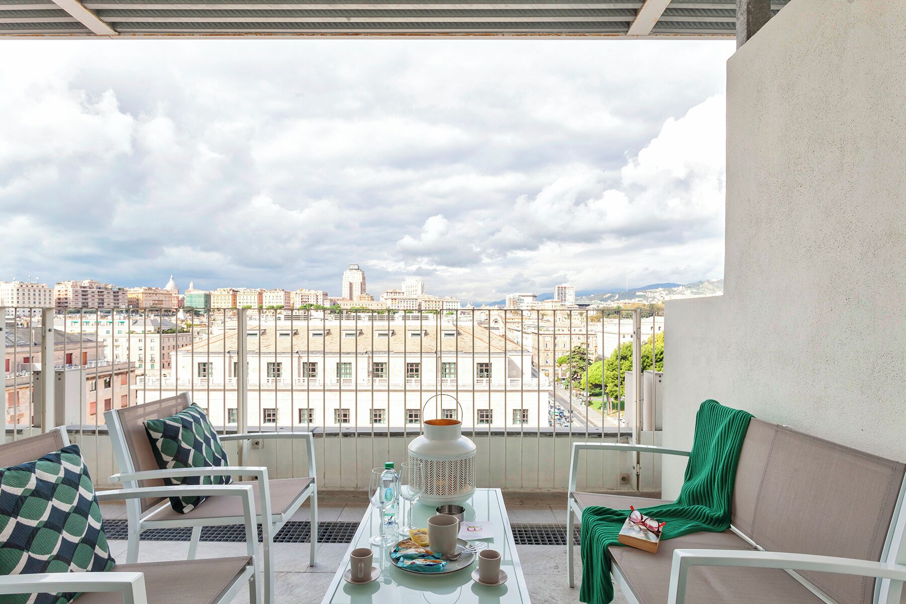 A balcony with a table set for two, chairs, and a view of a cityscape.