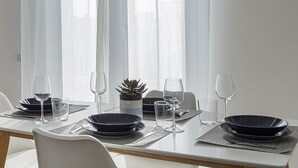 A dining table set with plates, glasses, and a small plant, with sheer curtains and a city view in the background. - Deluxe Apartments by Wonderful Italy (Genoa)