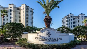 Schild für Clubhouse & Spa by Spectrum Resorts, mit der Nummer 453, umgeben von Palmen und blauem Himmel.