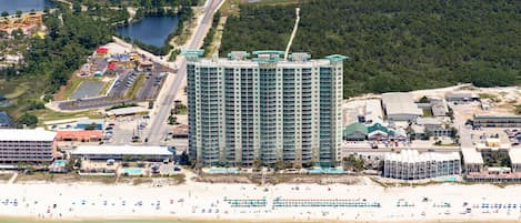 A high-rise hotel with a modern design, located near a beach and a parking area.