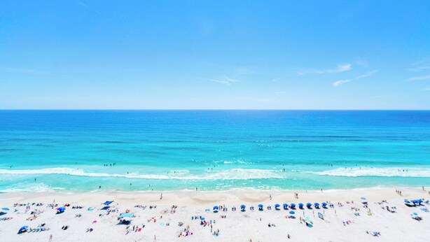 Une plage avec une eau d’un bleu limpide, un rivage sablonneux et des parasols.
