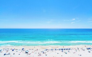 Ein Strand mit klarem, blauem Wasser, sandigem Ufer und Sonnenschirmen.