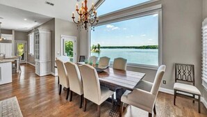 A dining area with a large window overlooking a lake, a chandelier, and a view of the kitchen. - Great Dock! Wifi, Propane Fire-Pit!  Come Visit "Dock Holiday"! (Huddleston)