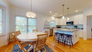Une cuisine moderne avec des meubles blancs, un îlot central doté de tabourets, et un coin repas avec une table ronde et des chaises.