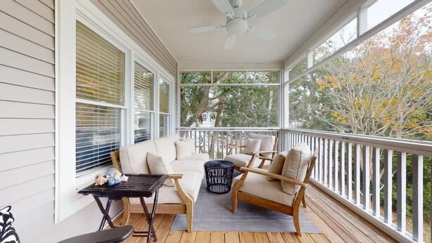 Une véranda couverte avec un ventilateur de plafond, une terrasse en bois et un espace détente comprenant une table et des chaises.