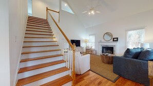 Un salon moderne avec un escalier en bois, une cheminée et une grande fenêtre.