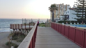 Une promenade en bois menant à une plage, d’où l’on a une vue sur l’océan, et un bâtiment doté de balcons.