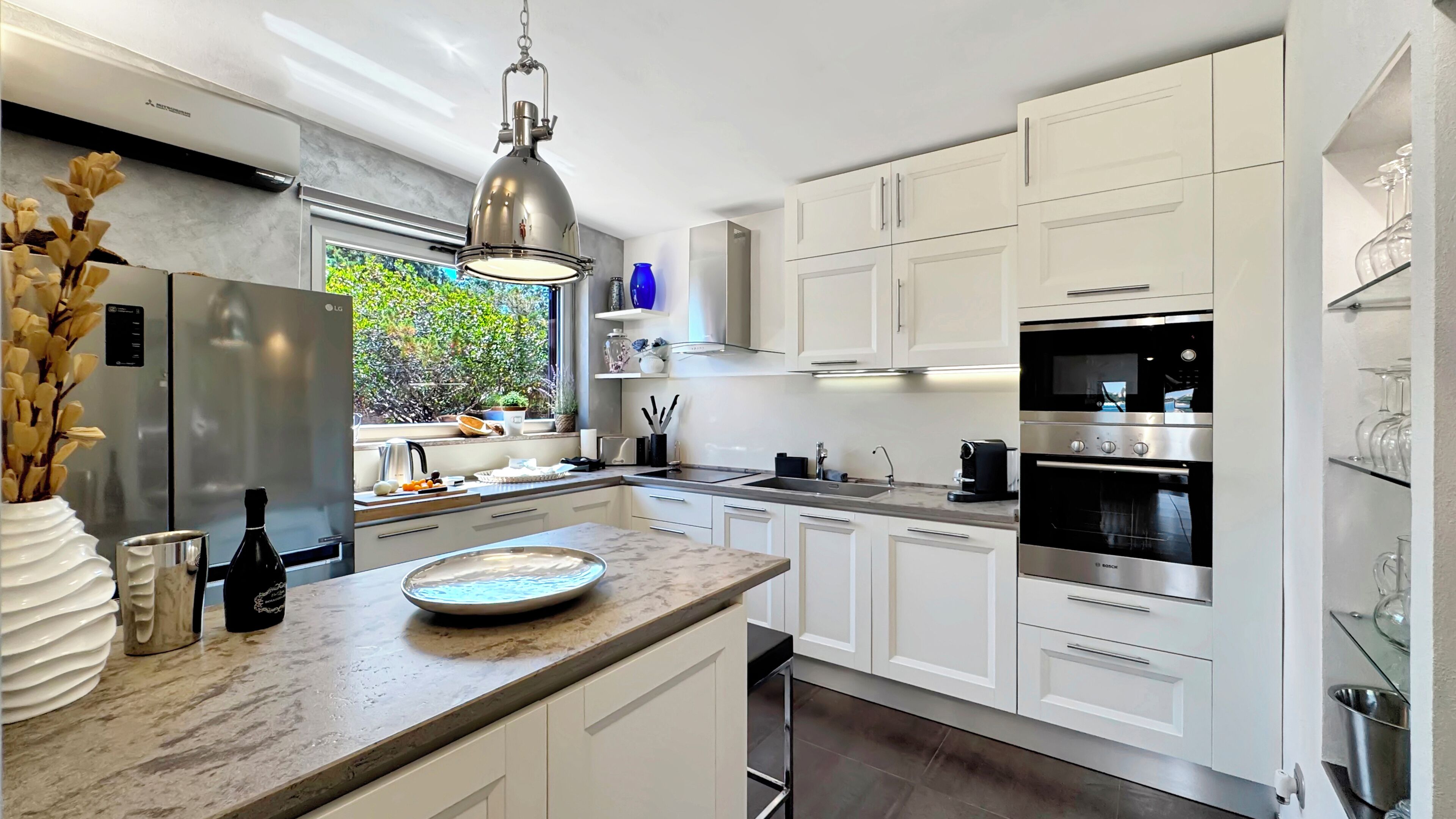 A modern kitchen with white cabinetry, stainless steel appliances, and a marble countertop.