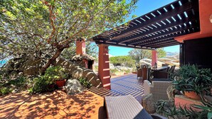 Een terras buiten met een pergola, zitplaatsen en potplanten.
