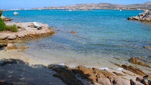 Un paysage côtier avec une eau turquoise et limpide, des rivages rocheux et des bateaux visibles au loin.