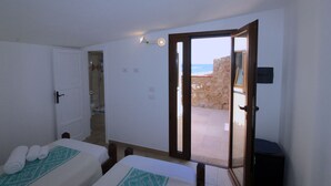A room with two beds, a bathroom, and a view of the sea through an open door. - Villa Iole (La Maddalena)