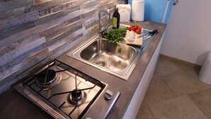 A modern kitchen with a stainless steel sink, a gas stove, and a wooden backsplash. - Villa Iole (La Maddalena)