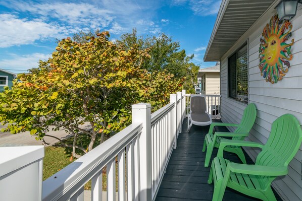 A porch with green Adirondack chairs, a white railing, and a colorful sun mural on the wall.