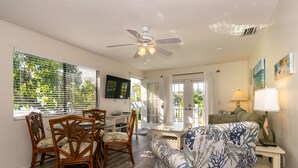 A living room with a ceiling fan, a dining table with chairs, a sofa, and a TV mounted on the wall.