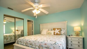 Un dormitorio con cama, mesita de noche, espejo y ventilador de techo.