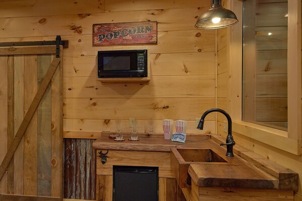 Una cocina rústica con paredes de madera, un microondas, un lavamanos y un cartel que dice 'Hot Popcorn Fresh'.