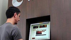 Una persona usando una computadora en un escritorio con un monitor, un teclado y un cartel informativo en la pared.