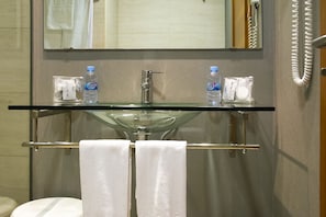 A bathroom with a glass sink, two bottles of Font Vella water, a towel rack with two towels, and a telephone.