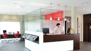 Zona de recepción de hotel con un separador de vidrio, un mostrador de recepción y un monitor de computadora.